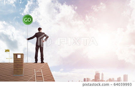 Businessman in suit on house top with ecology concept signboard. Mixed media Businessman in suit on house top with ecology concept signboard. Mixed media 64039993