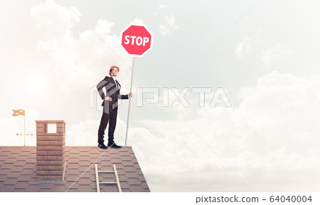 Caucasian businessman on brick house roof showing stop road sign Caucasian businessman on brick house roof showing stop road sign 64040004