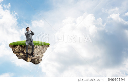 Young man on floating island in blue sky do not want to see anything Young man on floating island in blue sky do not want to see anything 64040194