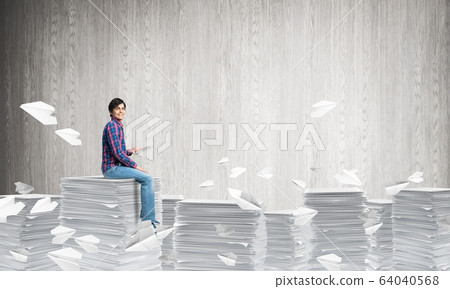 Attractive man sitting on pile of paper documents. Attractive man sitting on pile of paper documents. 64040568