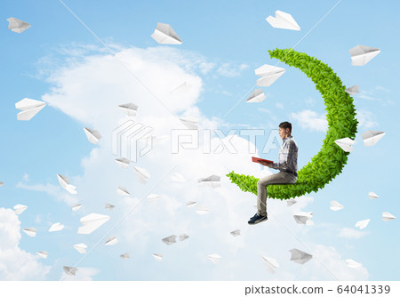 Handsome student guy sitting on green moon and reading book 64041339