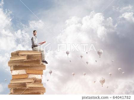 Man student on stack reading book and aerostats flying around 64041782