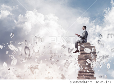 Man student on stack reading book and symbols flying around Man student on stack reading book and symbols flying around 64042165