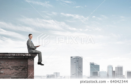 Man on roof edge reading book and cityscape at background Man on roof edge reading book and cityscape at background 64042344