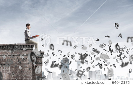 Man on roof edge reading book and symbols flying around Man on roof edge reading book and symbols flying around 64042375