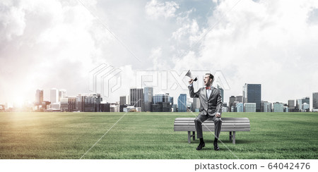Businessman in summer park announcing something in loudspeaker a Businessman in summer park announcing something in loudspeaker a 64042476