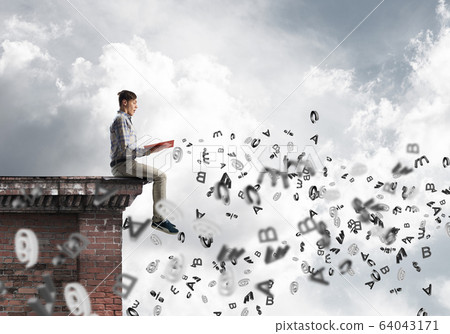 Man on roof edge reading book and symbols flying around 64043171