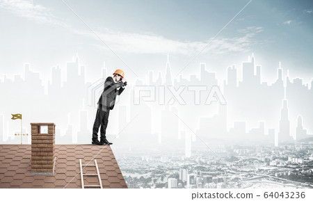 Engineer man standing on roof and looking in binoculars. Mixed m Engineer man standing on roof and looking in binoculars. Mixed m 64043236