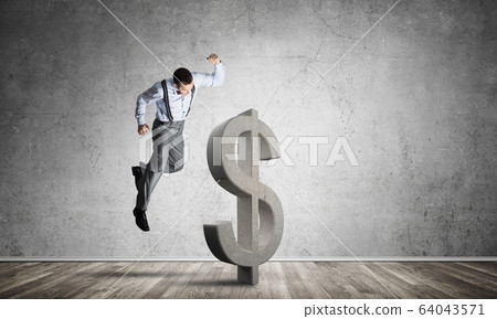 Determined banker man in empty concrete room breaking dollar figure 64043571