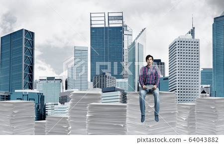 Attractive man sitting on pile of paper documents. Attractive man sitting on pile of paper documents. 64043882