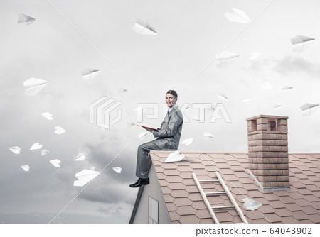 Man on brick roof reading book and paper planes flying in air Man on brick roof reading book and paper planes flying in air 64043902
