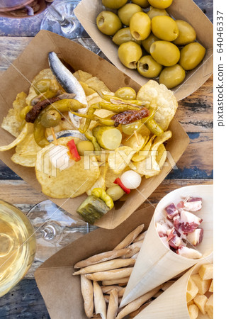 Tapas and pinchos. Spicy gildas with peppers, potato chips, olives, jamon on a wooden table in an outdoors cafe Tapas and pinchos. Spicy gildas with peppers, potato chips, olives, jamon on a wooden table in an outdoors cafe 64046337