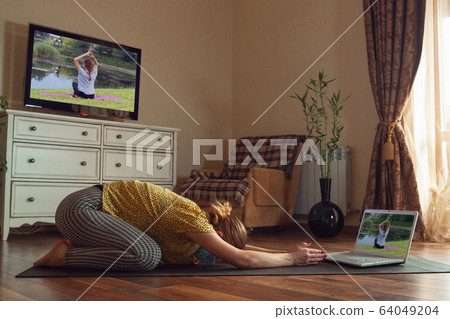 Sporty young woman taking yoga lessons online and practice at home while being quarantine Sporty young woman taking yoga lessons online and practice at home while being quarantine 64049204