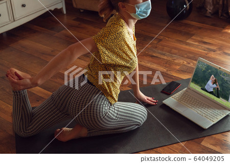 Sporty young woman taking yoga lessons online and practice at home while being quarantine Sporty young woman taking yoga lessons online and practice at home while being quarantine 64049205
