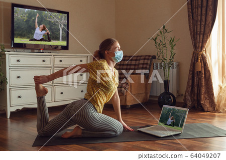 Sporty young woman taking yoga lessons online and practice at home while being quarantine Sporty young woman taking yoga lessons online and practice at home while being quarantine 64049207