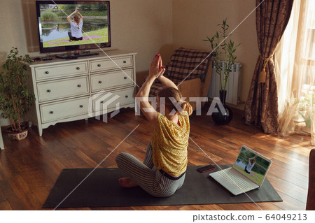 Sporty young woman taking yoga lessons online and practice at home while being quarantine Sporty young woman taking yoga lessons online and practice at home while being quarantine 64049213