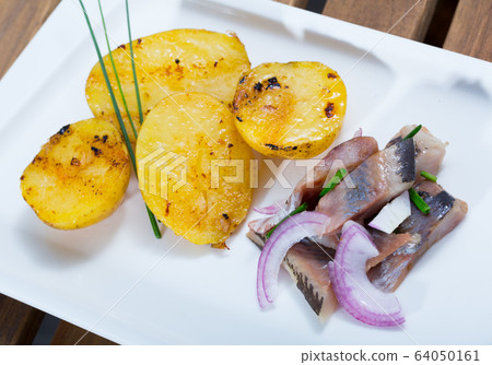 Fried potatoes with slices of mild-cured herring and onions served on plate Fried potatoes with slices of mild-cured herring and onions served on plate 64050161