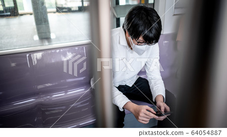 Asian man wearing mask using phone on skytrain Asian man wearing mask using phone on skytrain 64054887
