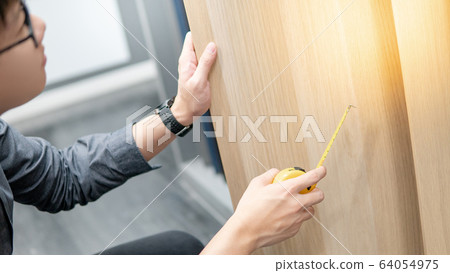 Asian man using tape measure on cabinet materials Asian man using tape measure on cabinet materials 64054975