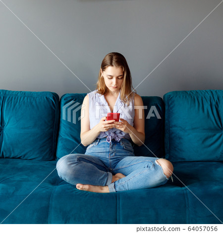 Young woman at home relaxing on the couch, using smartphone. Young woman at home relaxing on the couch, using smartphone. 64057056