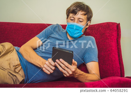 E-book and online education. A man is reading a quarantined book at home. A man in a medical mask E-book and online education. A man is reading a quarantined book at home. A man in a medical mask 64058291