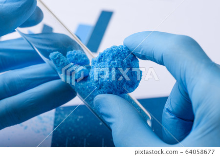 Scientist show blue crystal material in hand and glass test tube in laboratory 64058677
