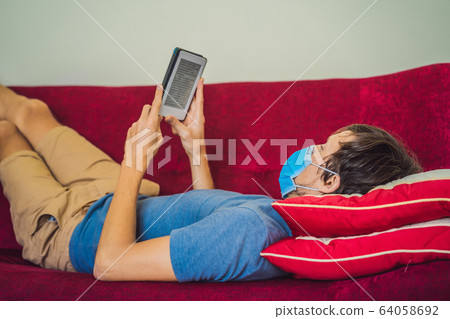 E-book and online education. A man is reading a quarantined book at home. A man in a medical mask E-book and online education. A man is reading a quarantined book at home. A man in a medical mask 64058692