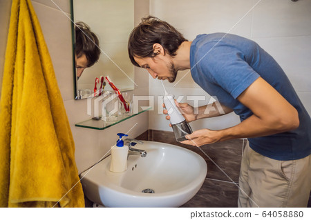 A man uses an oral irrigator in his bathroom A man uses an oral irrigator in his bathroom 64058880