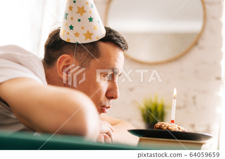 Thoughtful sad man sitting in front of little cake with lighted candle. 64059659