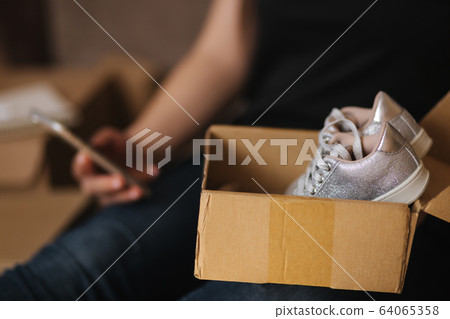 Young woman open new parcel with clothes. Woman hepl to sell secound hand goods Young woman open new parcel with clothes. Woman hepl to sell secound hand goods 64065358