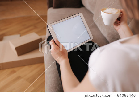 Woman shopping online at home use tablet. Woman work on tablet and drink cappuccino. Quarantine time. Boxes on the floor. Parcel Woman shopping online at home use tablet. Woman work on tablet and drink cappuccino. Quarantine time. Boxes on the floor. Parcel 64065446