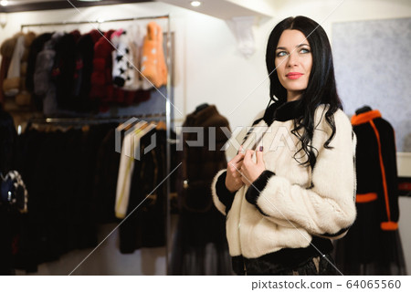 Attractive young woman choosing a fur coat from the hanger in the shop Attractive young woman choosing a fur coat from the hanger in the shop 64065560