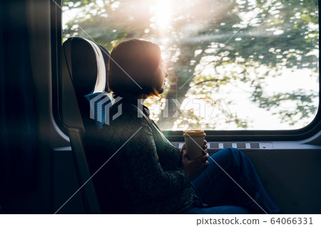 A woman sitting by the window of a commuter train with a laptop and coffee cup 64066331