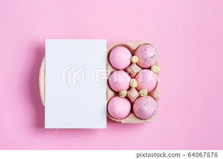 Paper container of craft pink painted Easter eggs and sheet of paper card on a same color background. 64067878