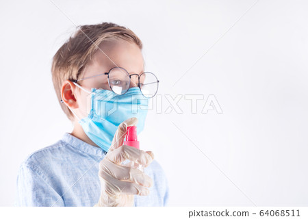 Small boy in a medical mask is holding antiseptic bottle in her hands against light grey background. 64068511