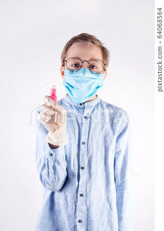 Small boy in a medical mask is holding antiseptic bottle in her hands against light grey background. 64068564