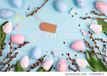 Decorative frame with Easter handcraft painted eggs, tulips flowers and paper label on a light blue background. 64069627
