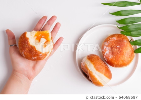 Homemade fresh doughnut with apricot jam in a woman hand and on a plate with palm leaves above white background Homemade fresh doughnut with apricot jam in a woman hand and on a plate with palm leaves above white background 64069687