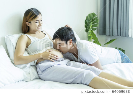 Husband kissing his wife’s belly in bed. Pregnant 64069688