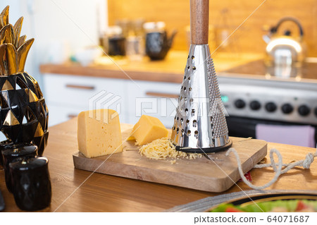 A piece of cheese on a wooden board next to an A piece of cheese on a wooden board next to an 64071687