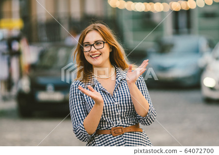 Street lights. Retro portrait young woman in checkered fashioned dress, bokeh of light bulbs on background. fun, smile, beautiful makeup. Poor vision and myopia. stylish woman at european street Street lights. Retro portrait young woman in checkered fashioned dress, bokeh of light bulbs on background. fun, smile, beautiful makeup. Poor vision and myopia. stylish woman at european street 64072700