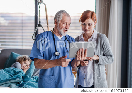 Doctor with tablet talking to mother of small hospitalized girl in hospital. 64073313