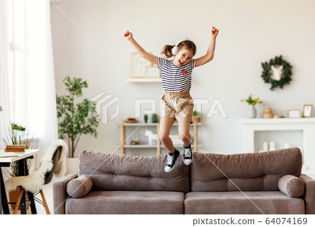 Happy girl listening to music and jumping on sofa. Happy girl listening to music and jumping on sofa. 64074169