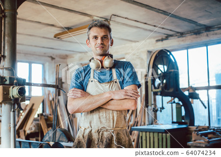 Carpenter standing in his wood workshop looking at camera 64074234