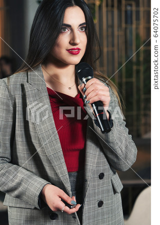 Business and speech topic: woman in a red shirt holding a black microphone, indoor Business and speech topic: woman in a red shirt holding a black microphone, indoor 64075702