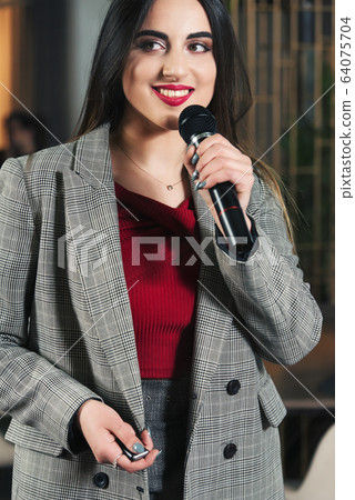 Business and speech topic: woman in a red shirt holding a black microphone, indoor Business and speech topic: woman in a red shirt holding a black microphone, indoor 64075704