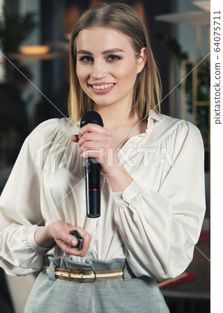 Business and speech topic: woman in a white blouse holding a black microphone, indoor Business and speech topic: woman in a white blouse holding a black microphone, indoor 64075711
