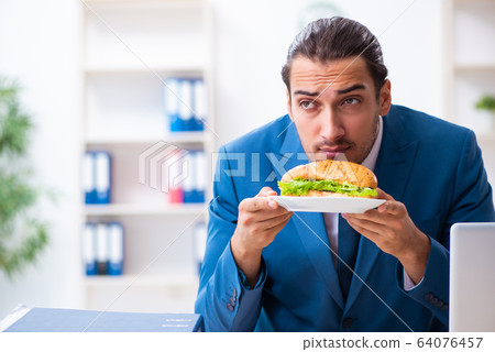 Young male employee having breakfast at workplace Young male employee having breakfast at workplace 64076457
