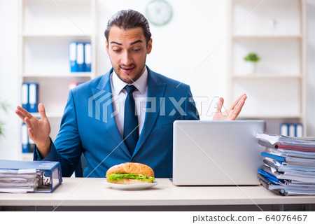 Young male employee having breakfast at workplace 64076467