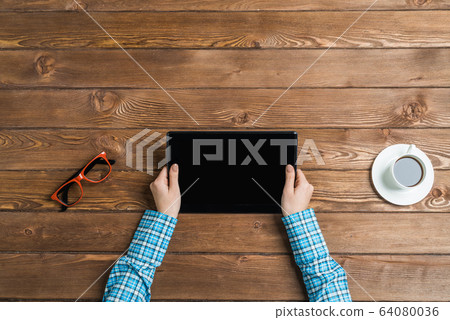 Top view of student sitting at wooden table and working with tablet 64080036
